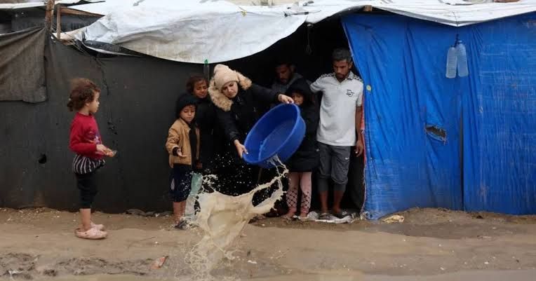 فلسطينية تحاول التخلص من المياه التي غمرت الخيمة التي تقطنها عائلتها<br alt=